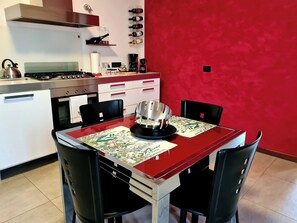 A kitchen with a red wall, a dining table with chairs, and a coffee machine. - CASA ANDREA PALLADIO - 72 m² apartment with private parking (Monticello Conte Otto)