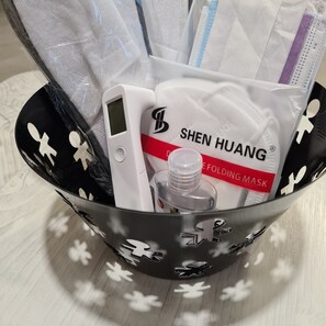 Una cesta negra con estampado floral que contiene una mascarilla facial, un protector facial y un accesorio para doblar mascarillas.
