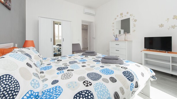 A bedroom with a bed, a TV, a dresser, and a door leading to another room. - Lilli Home Holidays Rome San Giovanni NOVEMBER OFFER (Roma)