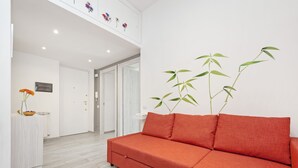 A modern living room with a red sofa, a white table with a vase of flowers, and a bamboo plant. - Lilli Home Holidays Rome San Giovanni NOVEMBER OFFER (Roma)