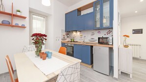 A modern kitchen with blue cabinets, a white refrigerator, and a dining area with a table and chairs. - Lilli Home Holidays Rome San Giovanni NOVEMBER OFFER (Roma)