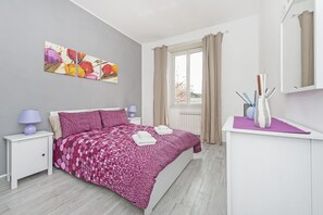 Ein Schlafzimmer mit Bett, Nachttisch, Kommode, einem Fenster mit Vorhängen und einem Bild an der Wand.