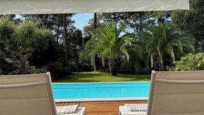 Un área junto a la piscina con sillones de descanso y una pérgola.