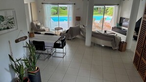Amplia sala de estar con vista a la piscina, un sofá, televisor y plantas en macetas.