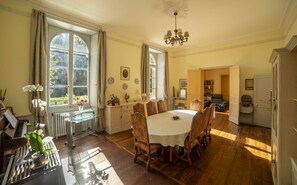 A dining room with a large table, chairs, a piano, and a radiator.
