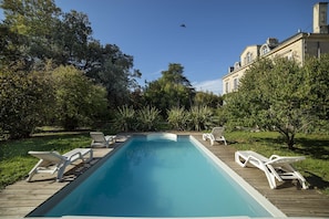 A rectangular swimming pool with a wooden deck and white lounge chairs.