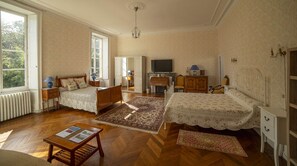 Ein geräumiges Zimmer mit zwei Betten, einem Fernseher, einem Kamin und einem großen Fenster mit Blick ins Freie.