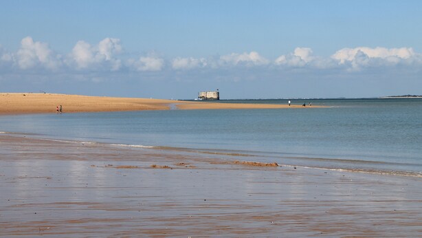 A beach with a sandy shore, a calm sea, and a distant building. - House with enclosed garden adjacent cycle path leading to the beach. Internet (Dolus-D'oléron)