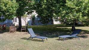 An outdoor seating area with wooden tables and chairs, and two lounge chairs under a tree. - House with enclosed garden adjacent cycle path leading to the beach. Internet (Dolus-D'oléron)