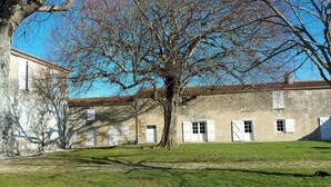A courtyard with a large tree, a building with multiple windows, and a clear blue sky. - House with enclosed garden adjacent cycle path leading to the beach. Internet (Dolus-D'oléron)