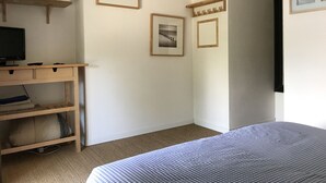 Un dormitorio con una cama, un escritorio con un ordenador y dos cuadros en la pared.