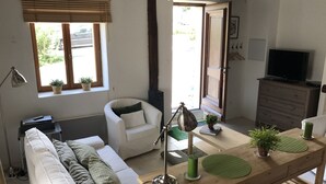 Una sala de estar acogedora con un sofá, una mesa de comedor de madera, una lámpara, un televisor y una ventana con persianas.