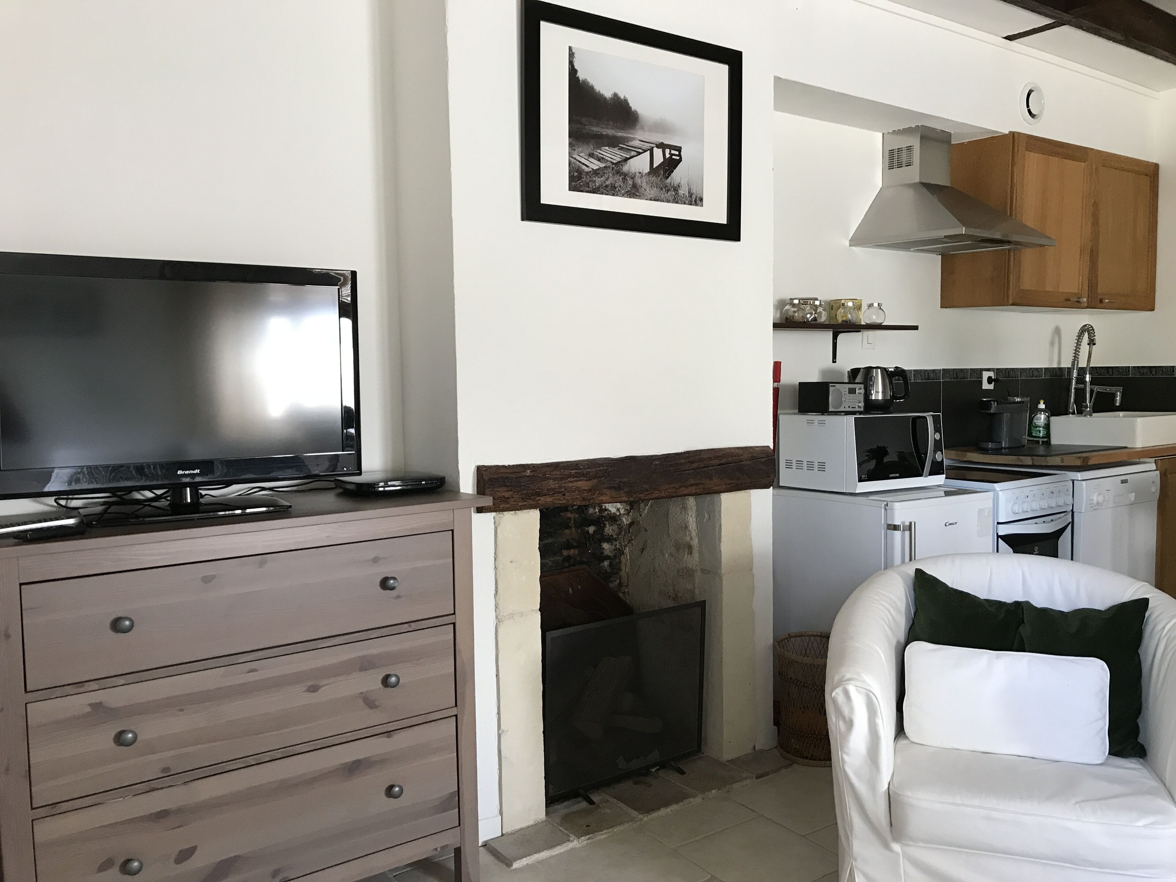 Een woonkamer met een flatscreen televisie, een houten kast, een open haard en een keuken met een magnetron, fornuis en kastjes.