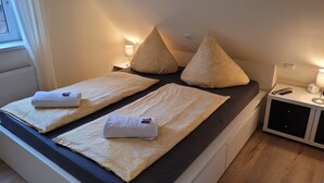 Un letto matrimoniale con due cuscini e due asciugamani piegati, un comodino con una lampada e un piccolo armadietto.