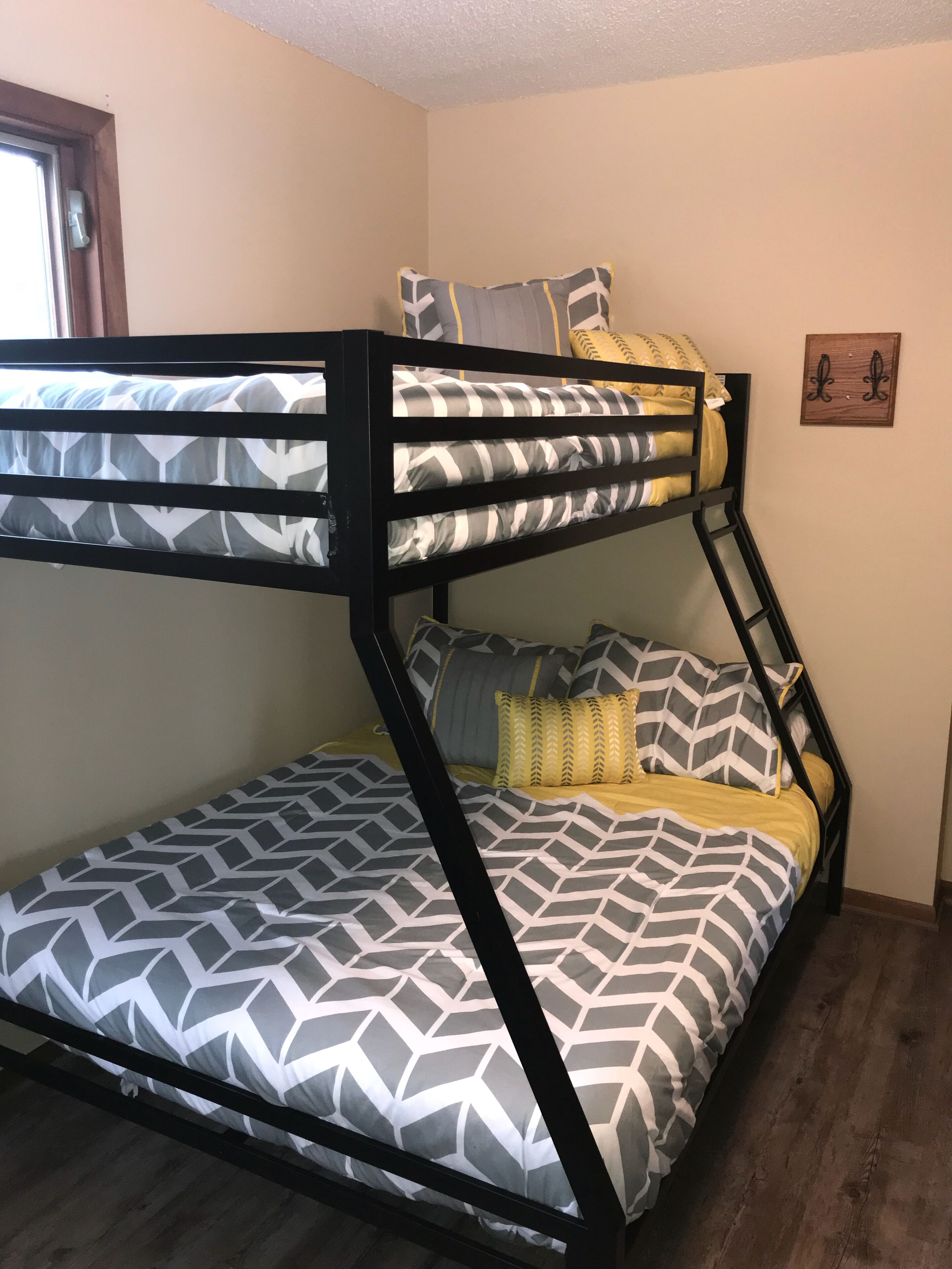 A bunk bed with geometric-patterned bedding, a wooden ladder, and a small wall decoration.