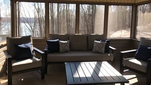 Un área de estar al aire libre techada con un sofá y dos sillones, ventanas amplias y ventilador de techo.