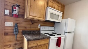 A kitchen with wooden cabinets, a white stove, a microwave, and a refrigerator. - Frenchy's Hideaways Cabin #3 (Custer)