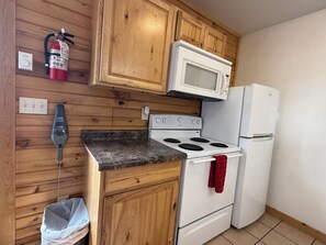 A kitchen with wooden cabinets, a white stove, a microwave, and a refrigerator.