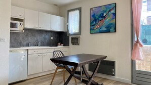 A compact kitchen with white cabinets, a microwave, and a dining table with chairs. - T2 apartment 100 meters bright, fully furnished baths (Gréoux-Les-Bains)