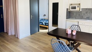 A compact kitchen with a microwave, sink, and cabinets. A dining table with chairs is in the foreground. - T2 apartment 100 meters bright, fully furnished baths (Gréoux-Les-Bains)