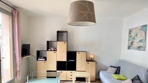 A modern living room with a sofa, a coffee table, a TV on a shelf, and a lamp. - T2 apartment 100 meters bright, fully furnished baths (Gréoux-Les-Bains)