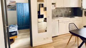 A compact kitchen with white cabinets, a sink, and a microwave. There's a dining table with chairs and a blue wardrobe in the adjacent room. - T2 apartment 100 meters bright, fully furnished baths (Gréoux-Les-Bains)