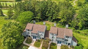 A two-story residential building with a brick facade and a symmetrical design, surrounded by lush greenery and a golf course in the background. - Beautiful Spacious 3BR/2BA Condo on The Grand Traverse Resort golf course (Williamsburg)