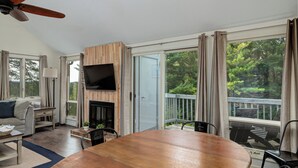 A spacious living room with a wooden dining table, a flat-screen TV mounted on a wooden wall, and a fireplace. - Beautiful Spacious 3BR/2BA Condo on The Grand Traverse Resort golf course (Williamsburg)