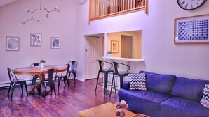 A modern living room with a dining area, a blue sofa, a wooden dining table, and a ceiling fan. - Beautiful Spacious 3BR/2BA Condo on The Grand Traverse Resort golf course (Williamsburg)