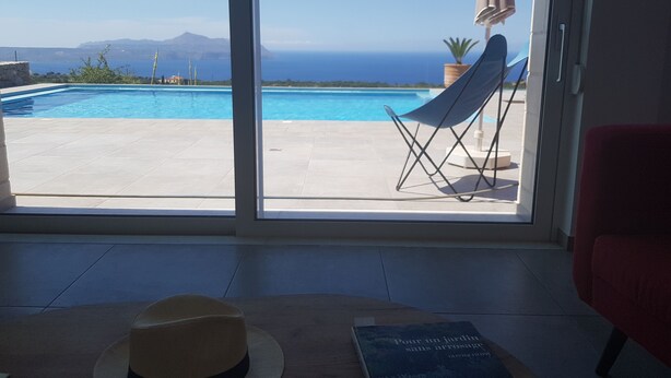 A view of a swimming pool with a chair and umbrella, a hat, and a book on a table. - Villa Cape Town design and tranquility in an enchanting (kokkino chorio)