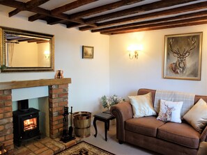 A cozy living room with a brick fireplace, a brown leather sofa, and a deer-themed pillow.
