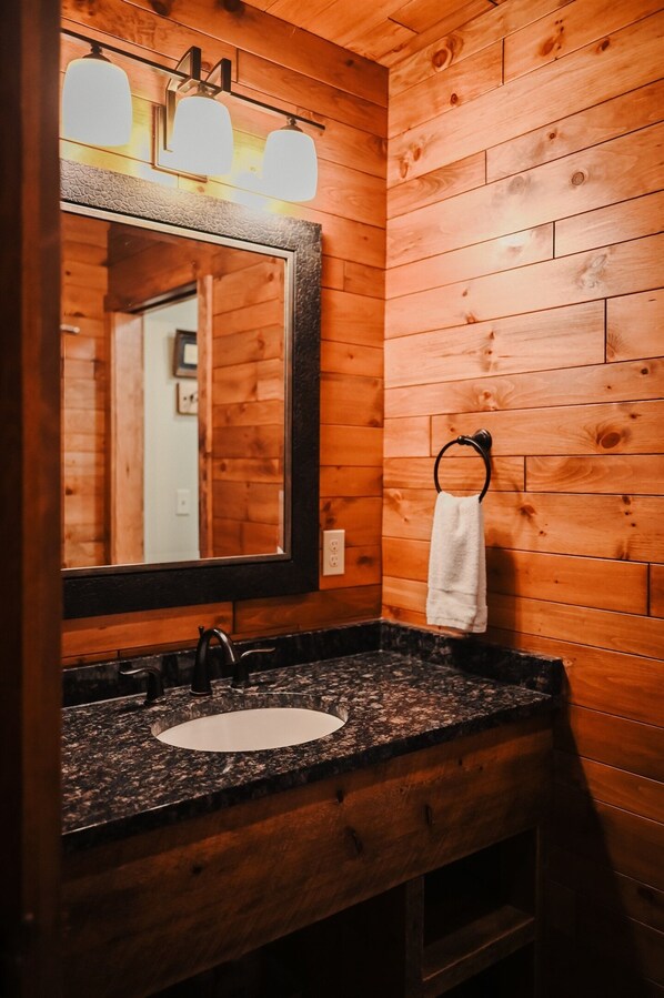 A wooden cabin-style bathroom with a granite countertop sink, a large mirror, and a towel ring.
