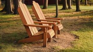 Kaksi puista Adirondack-tuolia puistossa, taustalla näkyy puita ja rakennus.