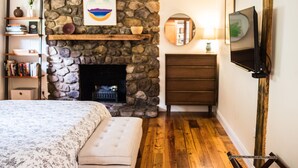 Ein Schlafzimmer mit Kamin aus Stein, einem Bett mit floralem Bettzeug, einem Holzkleiderschrank und einem an der Wand befestigten Fernseher.