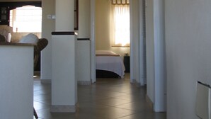 Um corredor com uma cama, uma mesa de cabeceira e uma janela com cortinas.