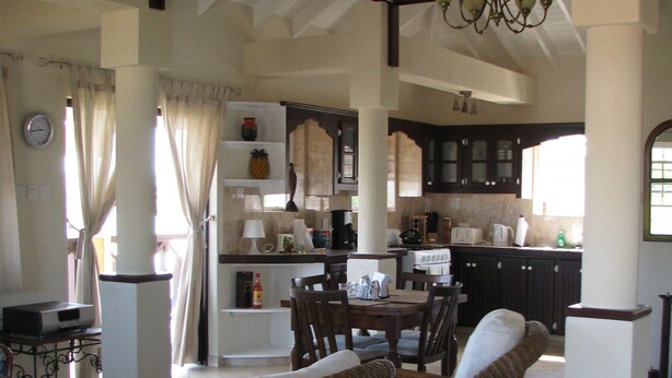 Uma cozinha espaçosa com armários de madeira escura, uma área de jantar com uma mesa grande e cadeiras, e uma sala de estar com um sofá e uma mesa de centro.
