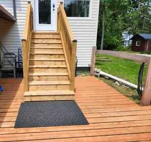 A wooden staircase leading to a white door, surrounded by a wooden deck and a grassy yard. - Unique Air-Conditioned Balsam Lake Waterfront,5 Bedrooms, 3 Baths, Dog friendly. (Kirkfield)