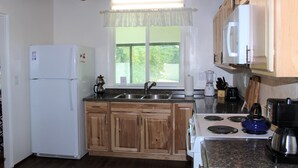 A kitchen with wooden cabinets, a white refrigerator, a stove, and a window with a view of greenery. - 3  Bedroom Home With Lovely Vigas And Wood Floors - 3.5 Miles To Santa Fe Plaza! (Santa Fe)