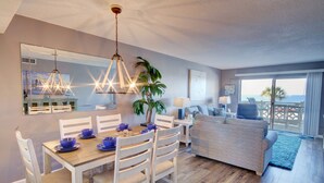 A modern living room with a dining area, a large window with a view, and a ceiling light fixture. - El Matador 332 -  FREE TICKETS!! Your stay includes free tickets to many area attractions! (Fort Walton Beach)