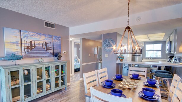 A dining area with a wooden table set for four, blue bowls, and a cabinet with glass doors. - El Matador 332 -  FREE TICKETS!! Your stay includes free tickets to many area attractions! (Fort Walton Beach)
