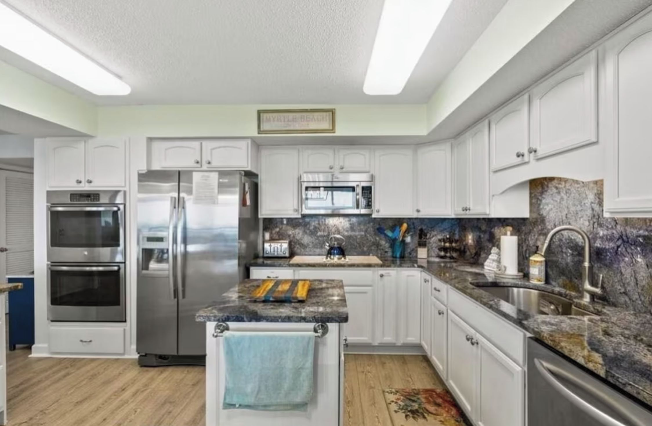 A modern kitchen with stainless steel appliances, white cabinetry, and a granite countertop.