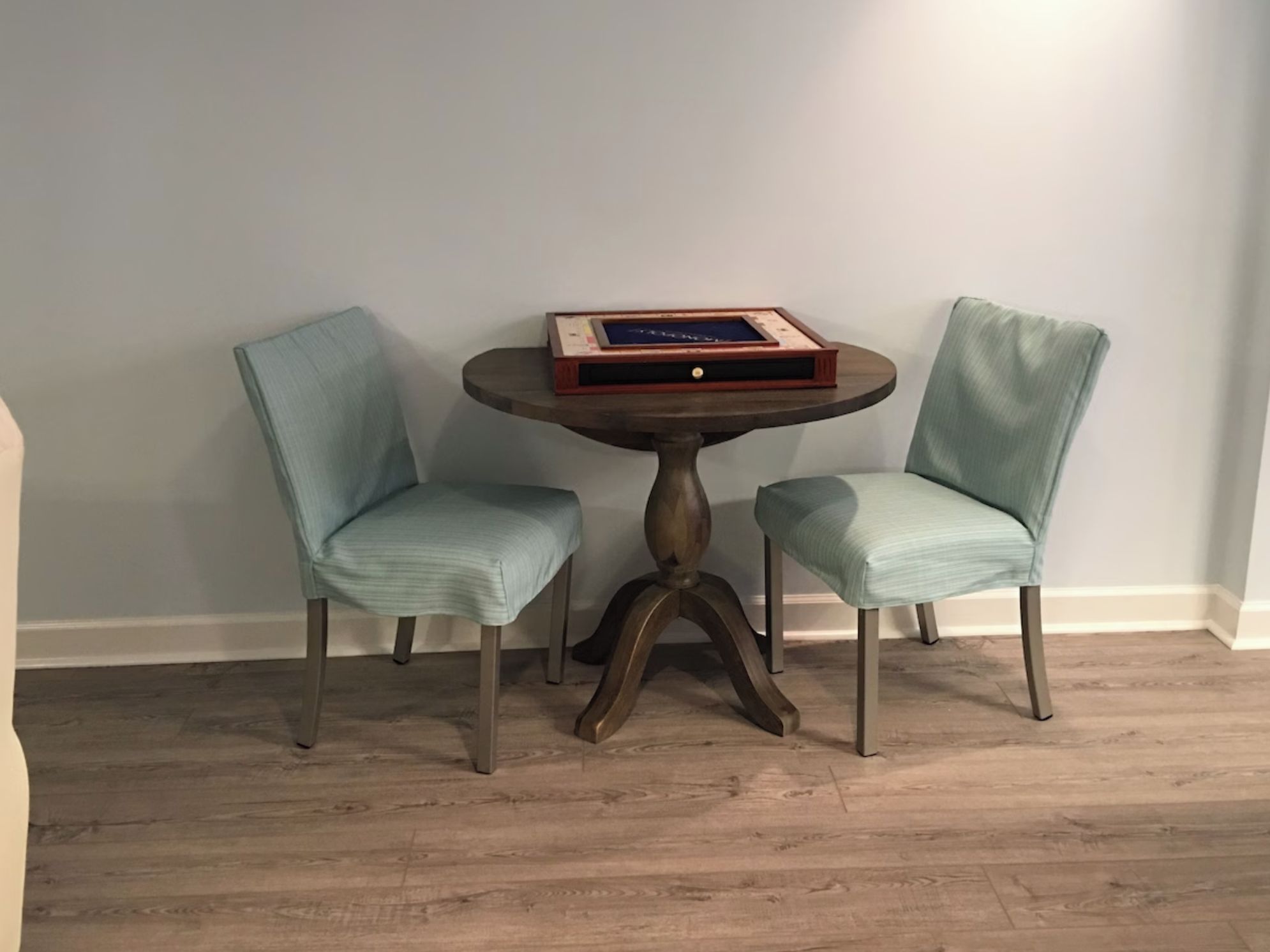 Une petite table ronde sur laquelle repose un livre, entourée de deux fauteuils rembourrés recouverts d’un tissu bleu clair.