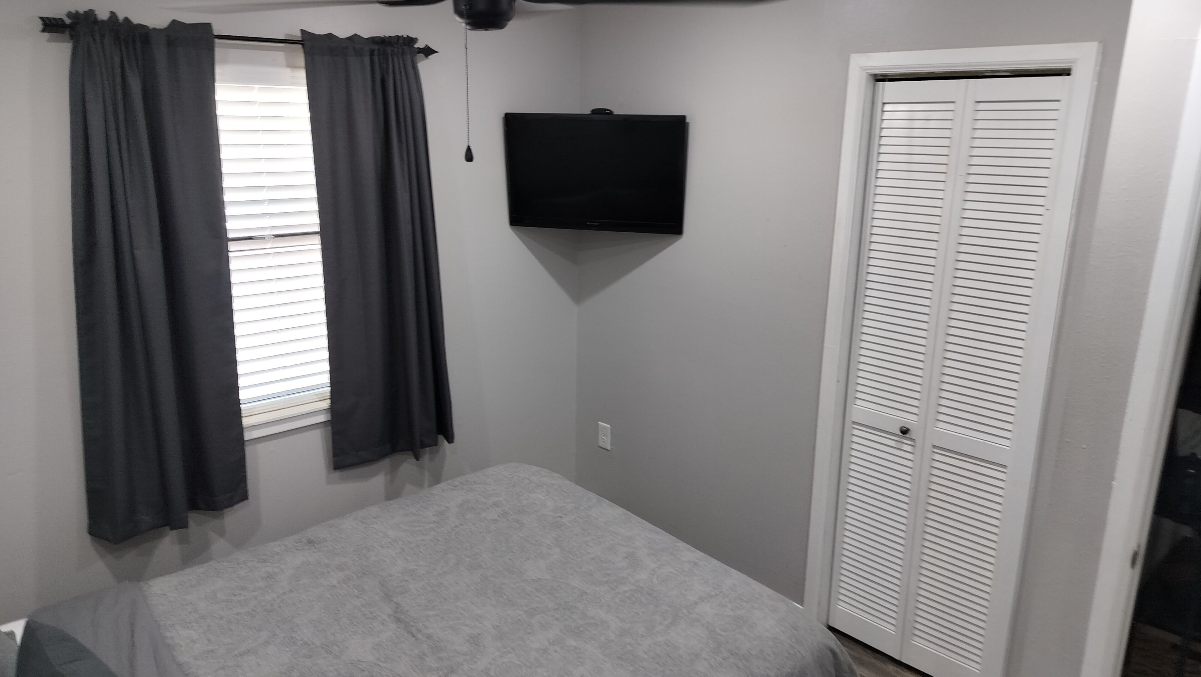 Een slaapkamer met een bed, een tv aan de muur, een kledingkast en een raam met gordijnen.