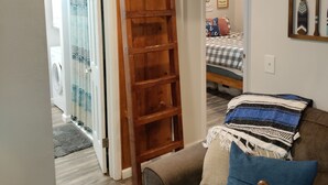 Una sala de estar acogedora con una estantería de madera, un sofá con un cojín azul y una cama con una colcha a cuadros.