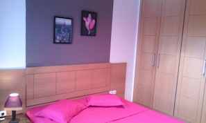 A bedroom with a bed, a nightstand, a lamp, a wardrobe, and two framed pictures on the wall.