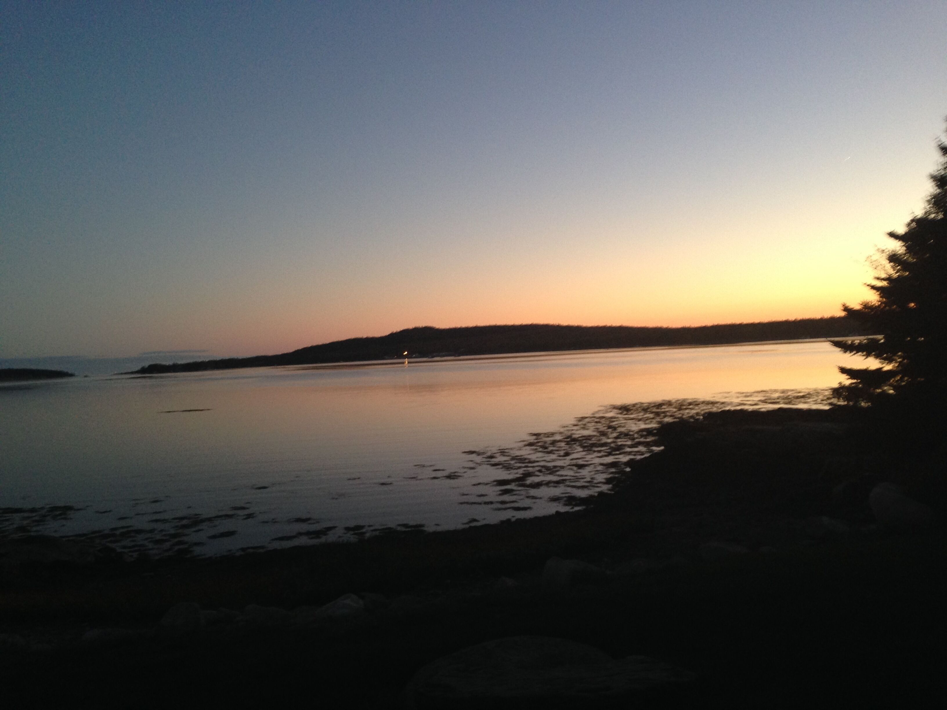 A calm body of water during sunset with a distant shoreline and a small boat.