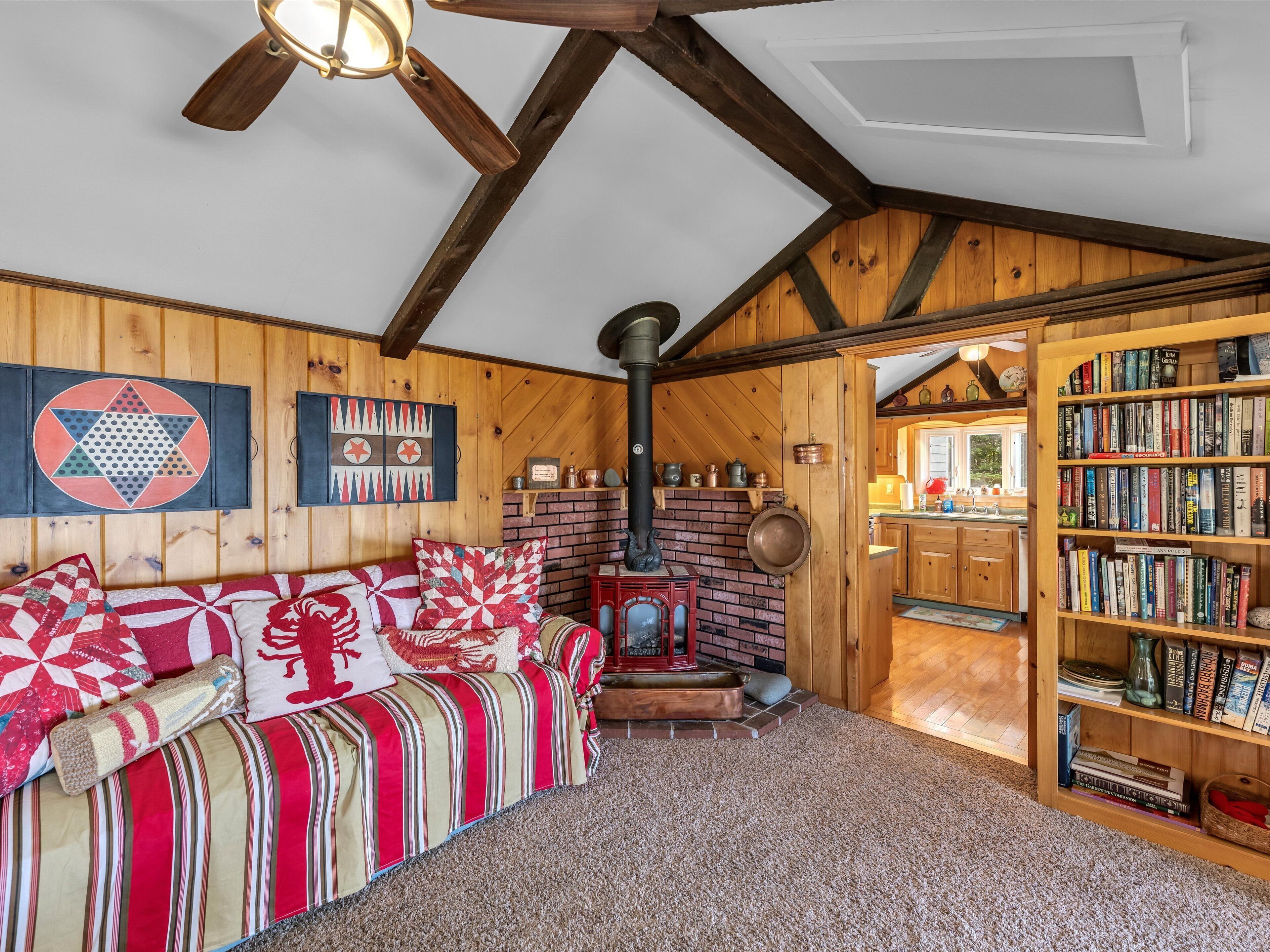 A cozy room with a wooden ceiling, a fireplace, a bookshelf, and a sofa with patterned cushions.