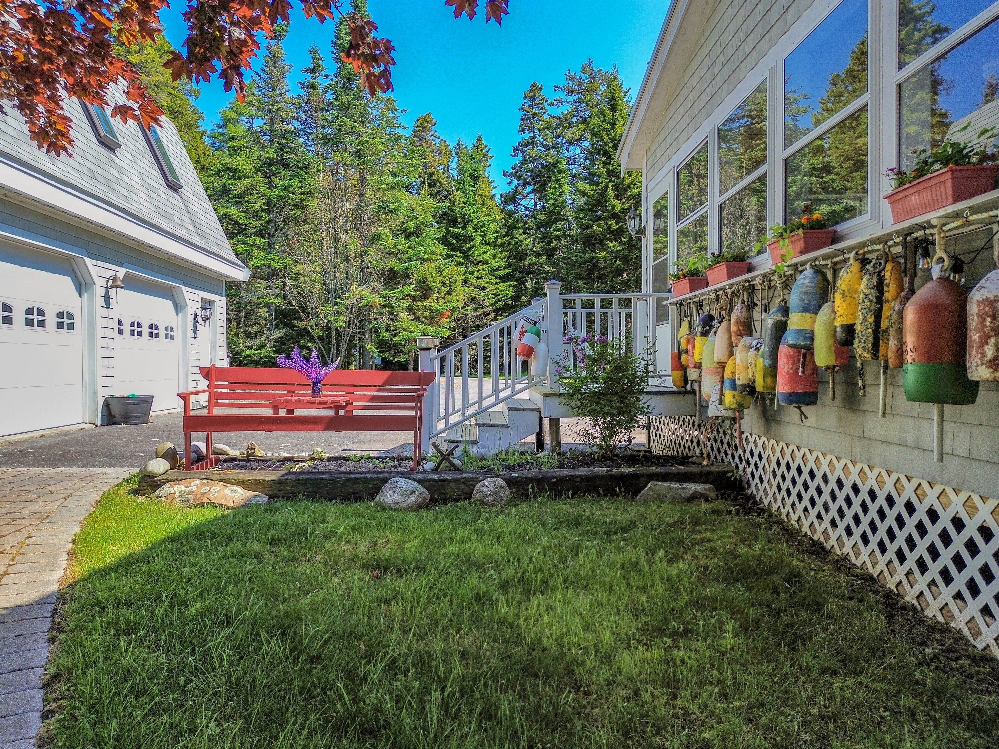 A house with a garage, a red bench, a small tree, and colorful buoys on the wall.