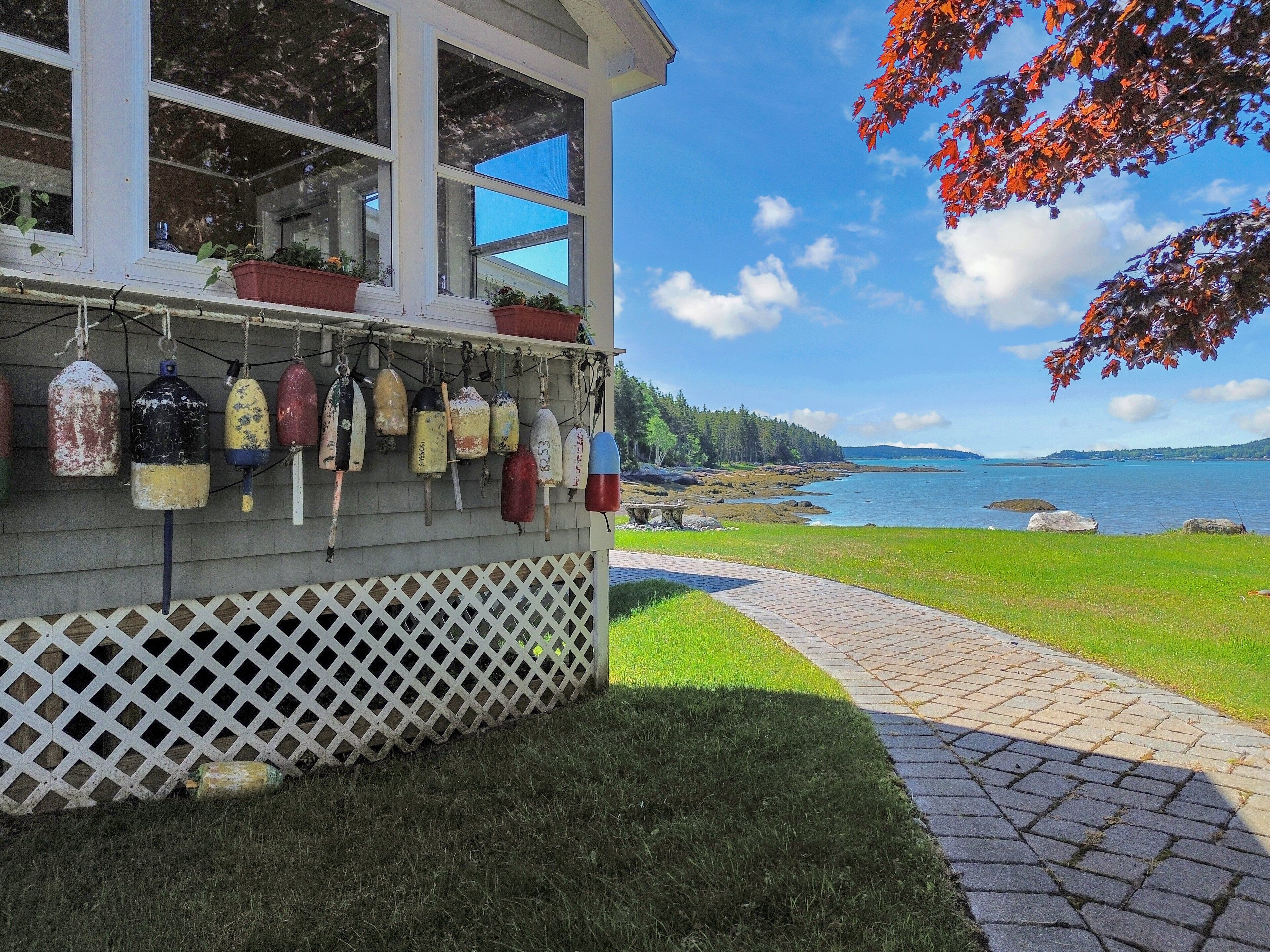 A building with a wooden lattice front, a pathway leading to a body of water, and buoys hanging on the exterior wall.