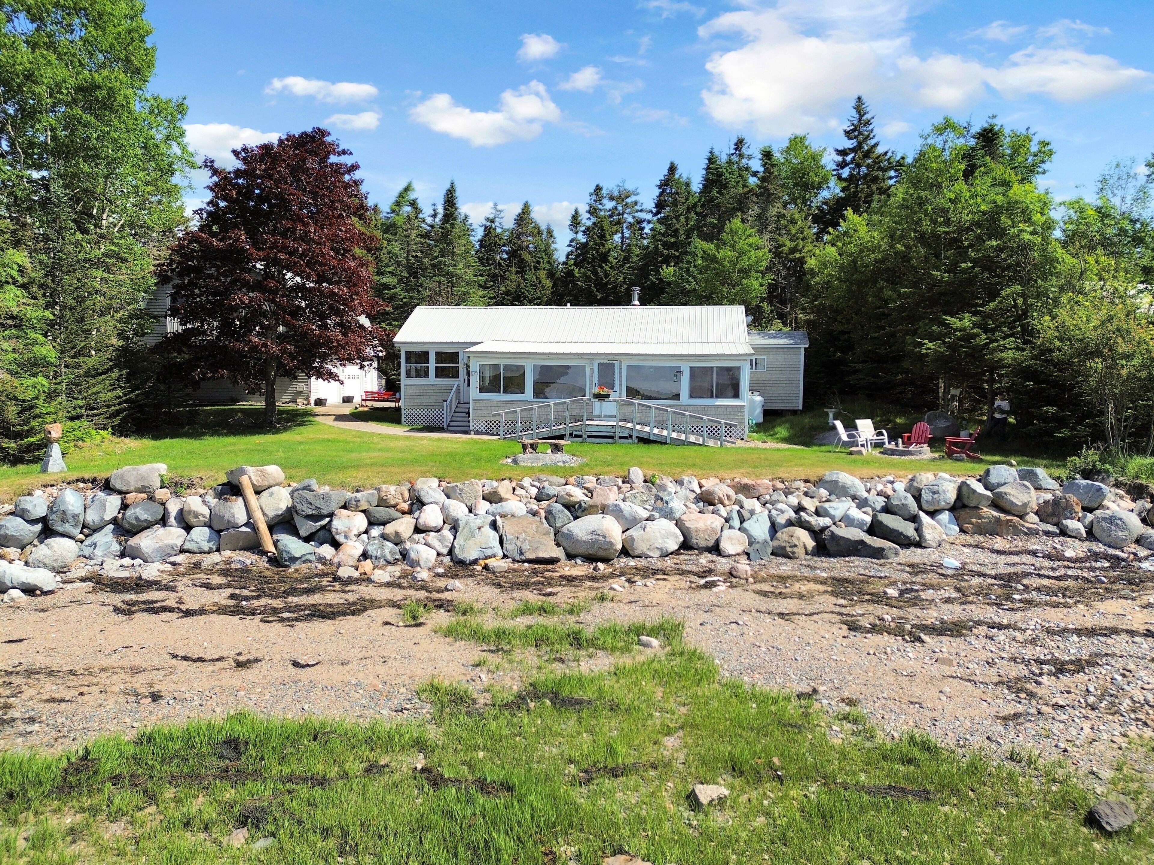 A coastal house with a porch, surrounded by a rocky shoreline and dense forest.